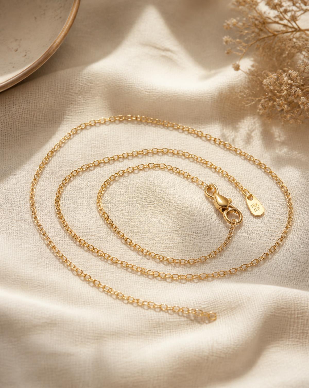 Lumière fine gold chain necklace coiled on cream linen