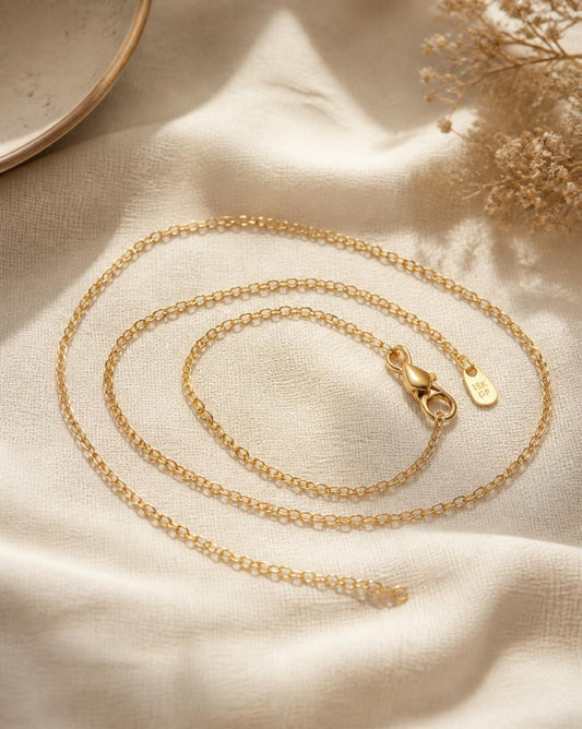 Lumière fine gold chain necklace coiled on cream linen