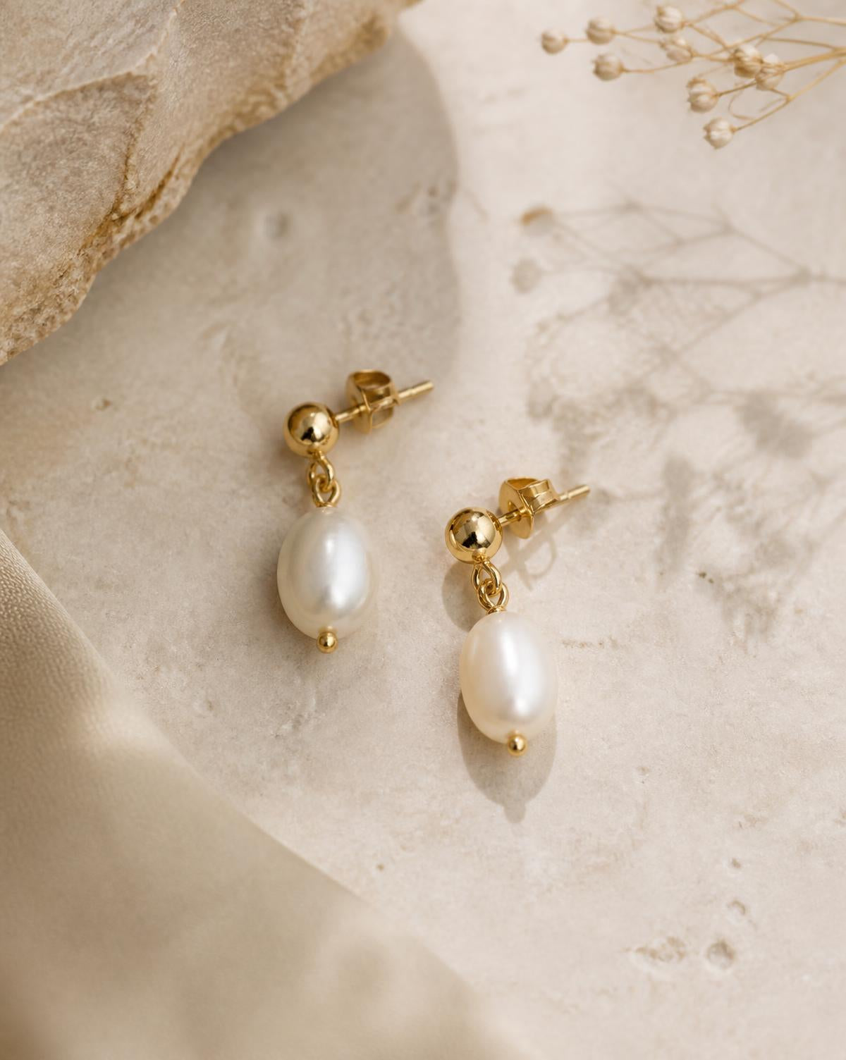 Perla freshwater pearl drop earrings in gold on cream stone
