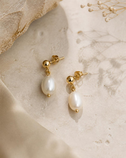 Perla freshwater pearl drop earrings in gold on cream stone